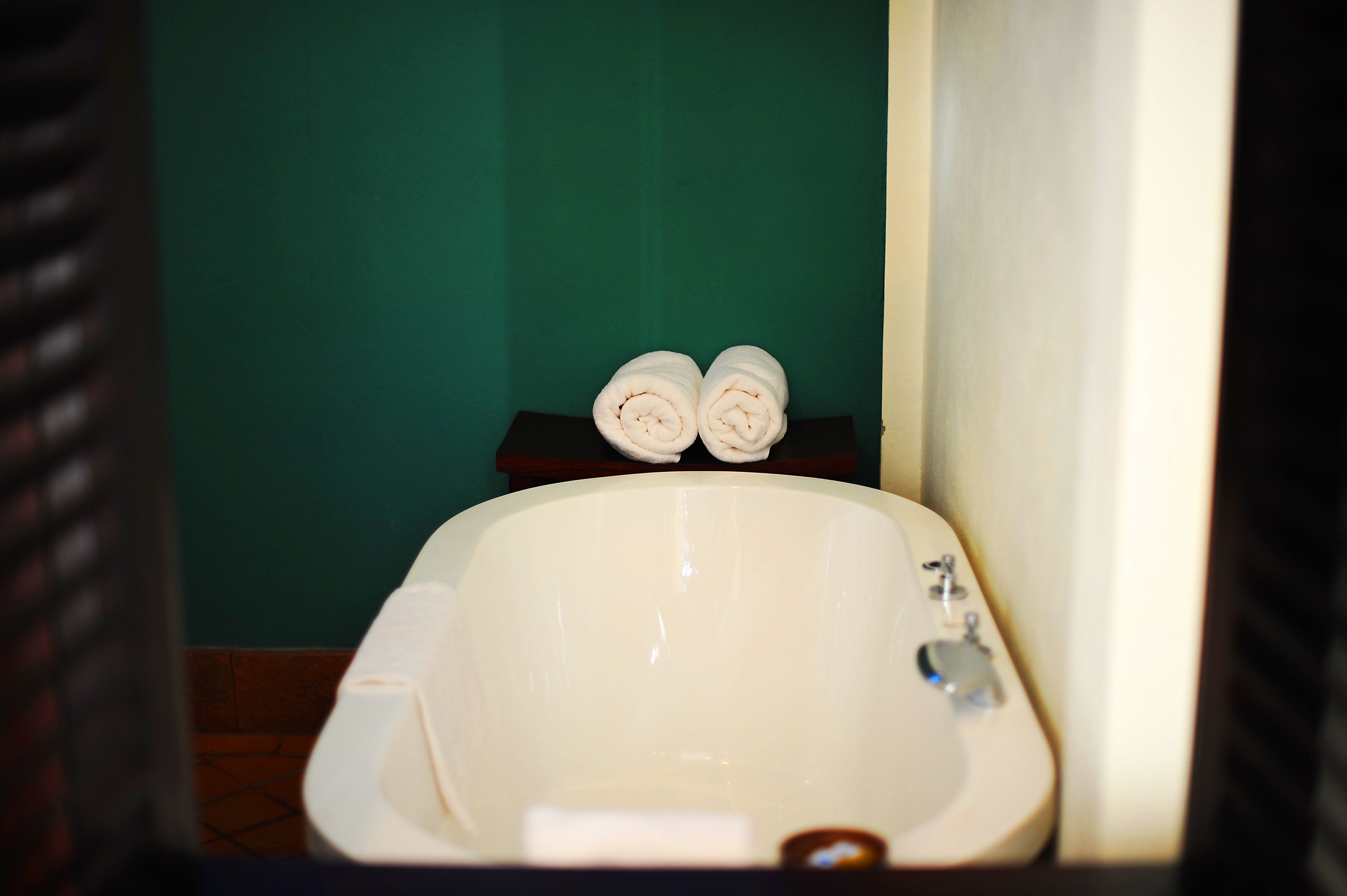 A bathroom with a white bathtub, a green wall, and a small shelf with two rolled towels.