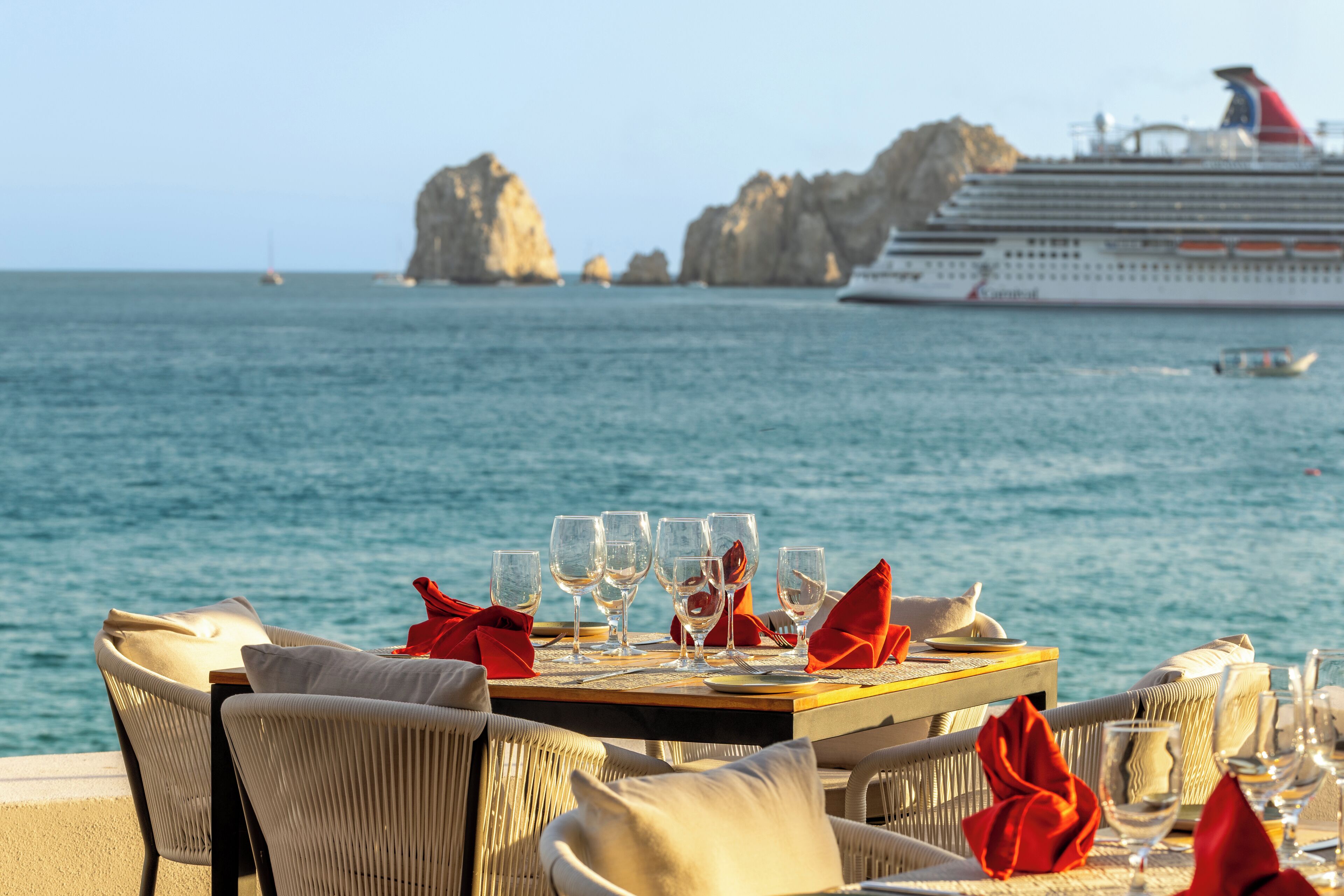 A dining table set with glasses and cutlery, overlooking the sea with a cruise ship in the background.