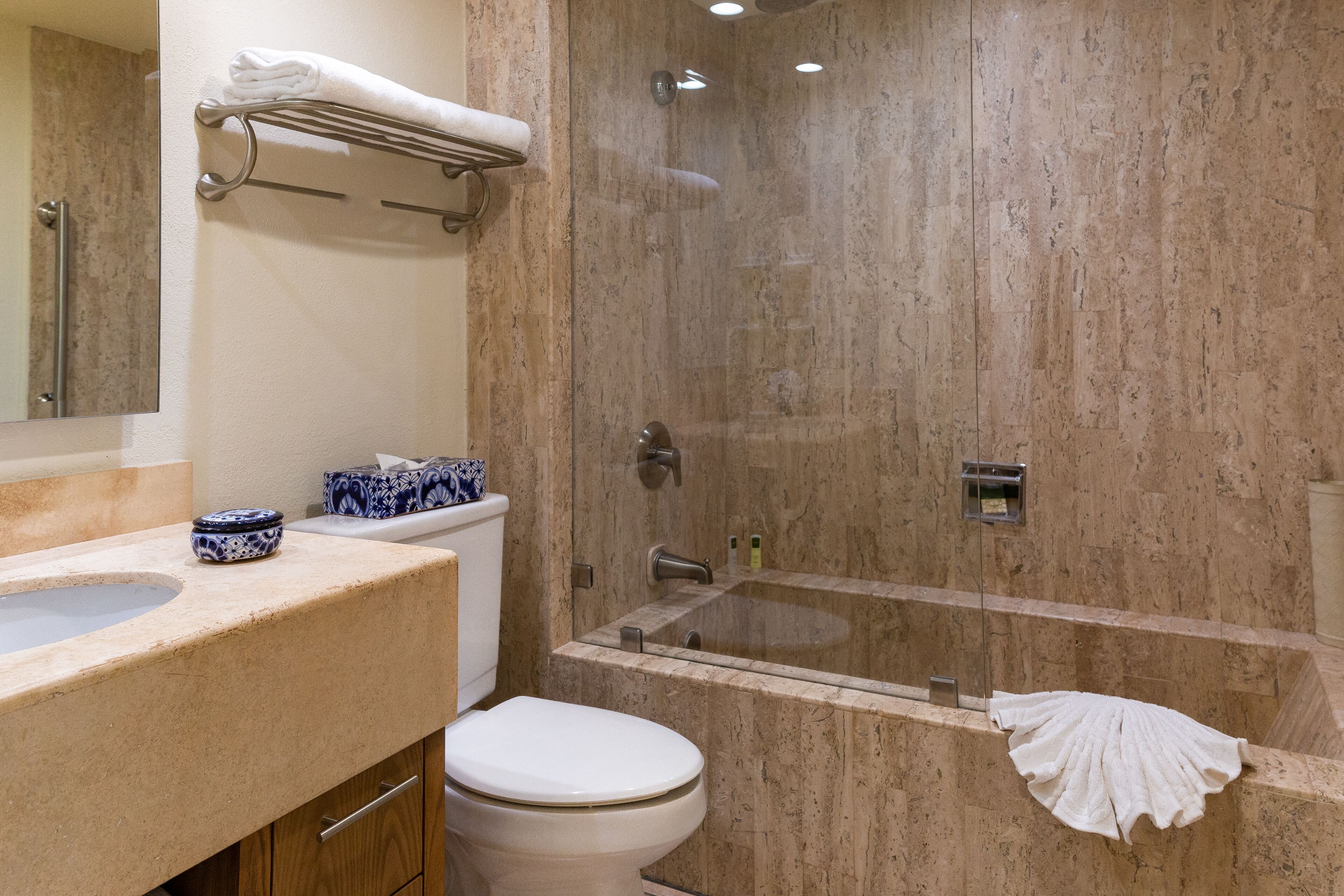 A bathroom with a marble wall, a glass-enclosed shower, a toilet, and a sink with a towel rack above it.