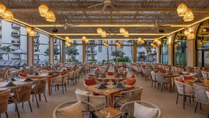 Een ruim restaurant met meerdere eettafels en stoelen, grote ramen met uitzicht op de omgeving en hangende pendelverlichting.