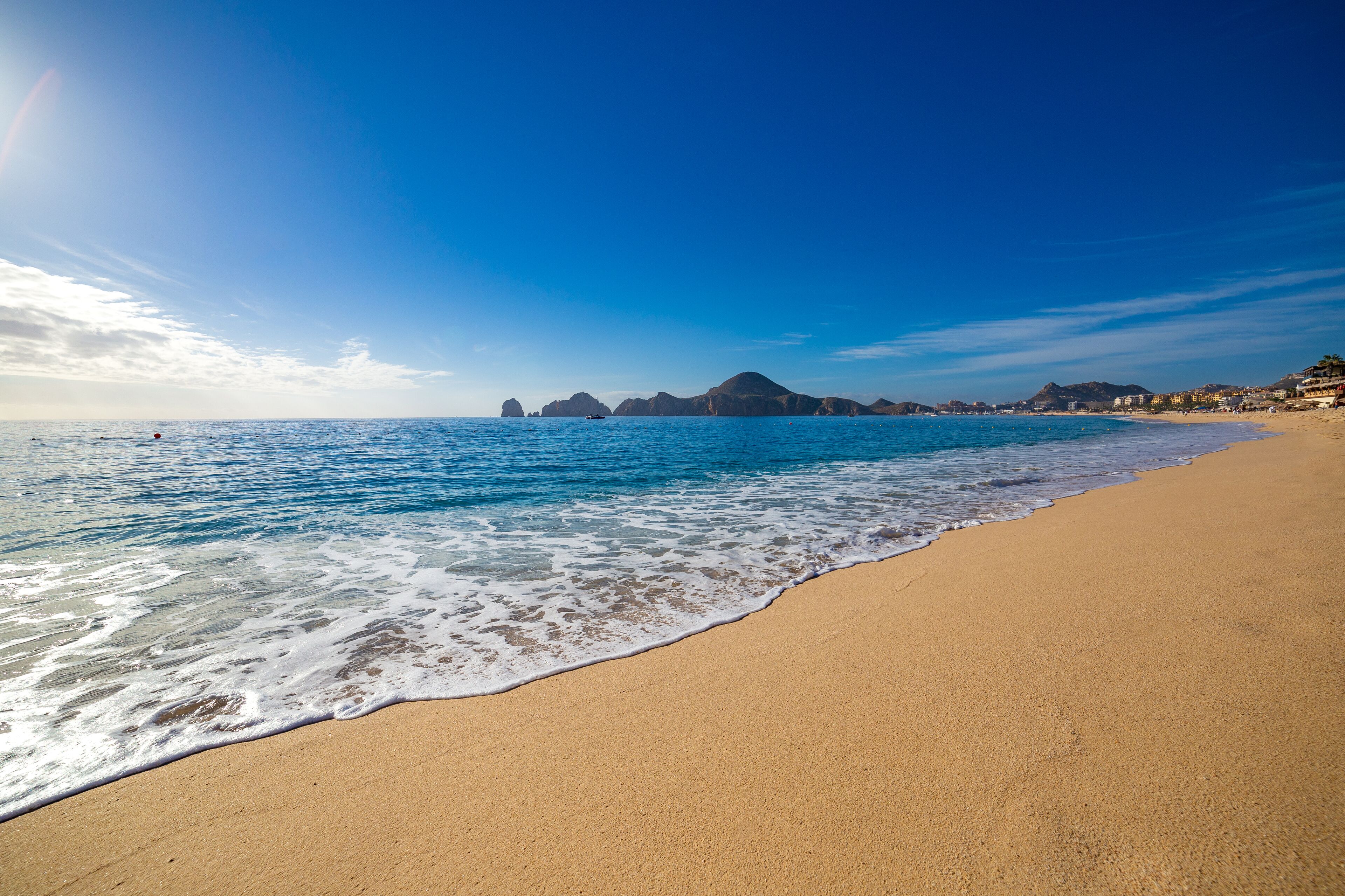Una playa con aguas cristalinas, una orilla arenosa y formaciones rocosas a lo lejos.