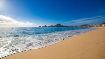 Una playa con aguas cristalinas, una orilla arenosa y formaciones rocosas a lo lejos.