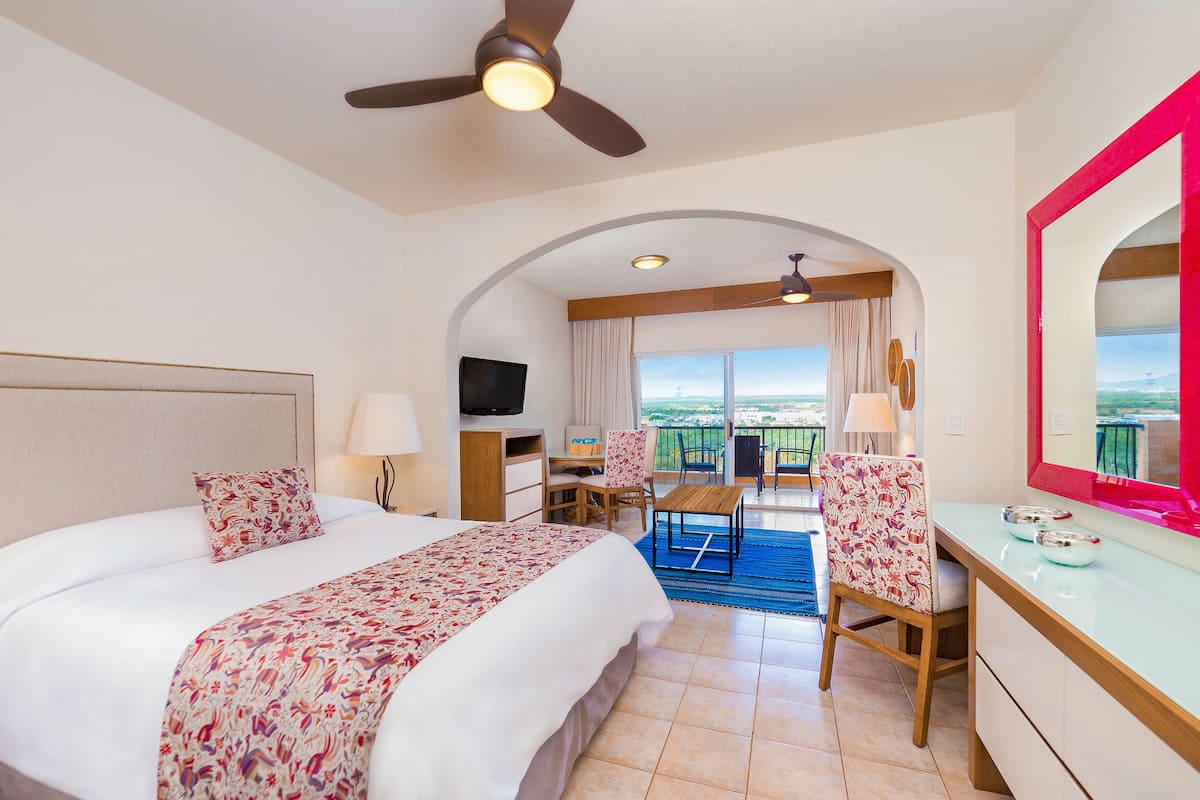A hotel room with a bed, desk, chair, and a balcony with a view.