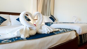 Habitación de hotel con dos camas, cada una con ropa blanca y almohadas azules. En la cama del primer plano, hay una decoración de toallas con forma de cisne.