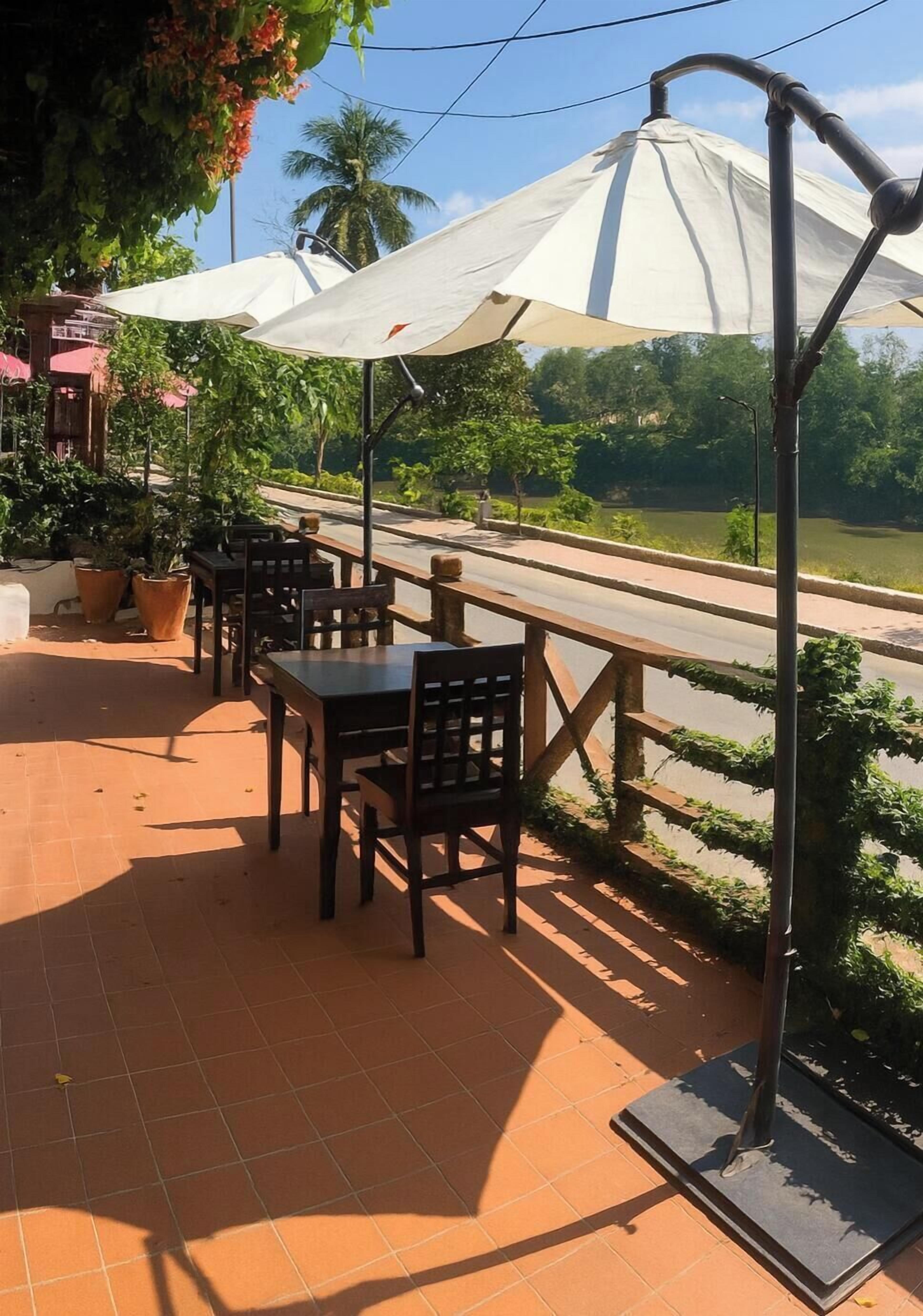 An outdoor seating area with tables and chairs, a white umbrella, and a view of a body of water.