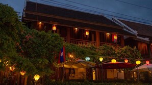 Un edificio de madera tradicional con un balcón, rodeado de vegetación e iluminado por faroles.