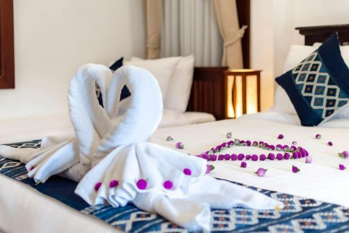 Habitación de hotel con cama, almohadas, mesita de noche y un arreglo decorativo de toallas y flores.