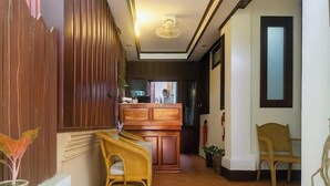 Un pasillo con mostrador de recepción, sillas de mimbre, plantas en macetas y piso de baldosas.
