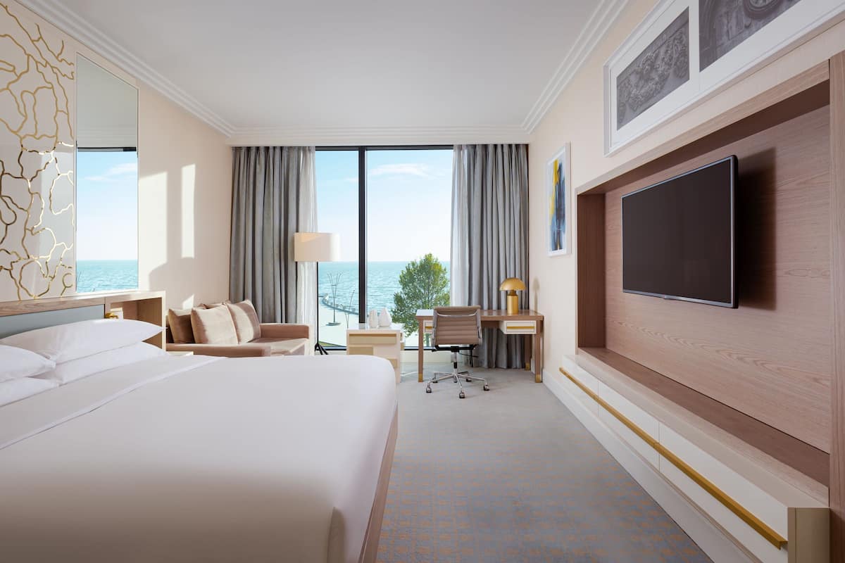 Habitación de hotel con una cama grande, un escritorio, una silla, un televisor y vista al mar.