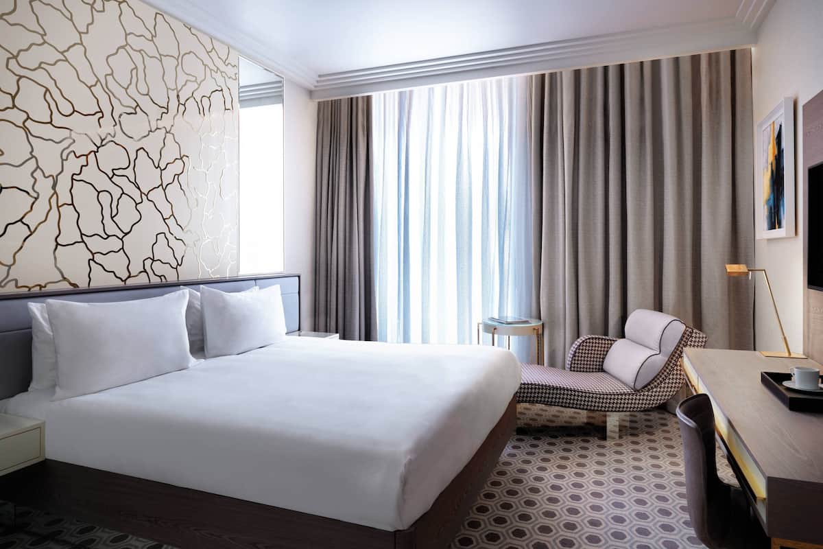 Una habitación de hotel con una cama grande, una mesita pequeña, una silla y un televisor.