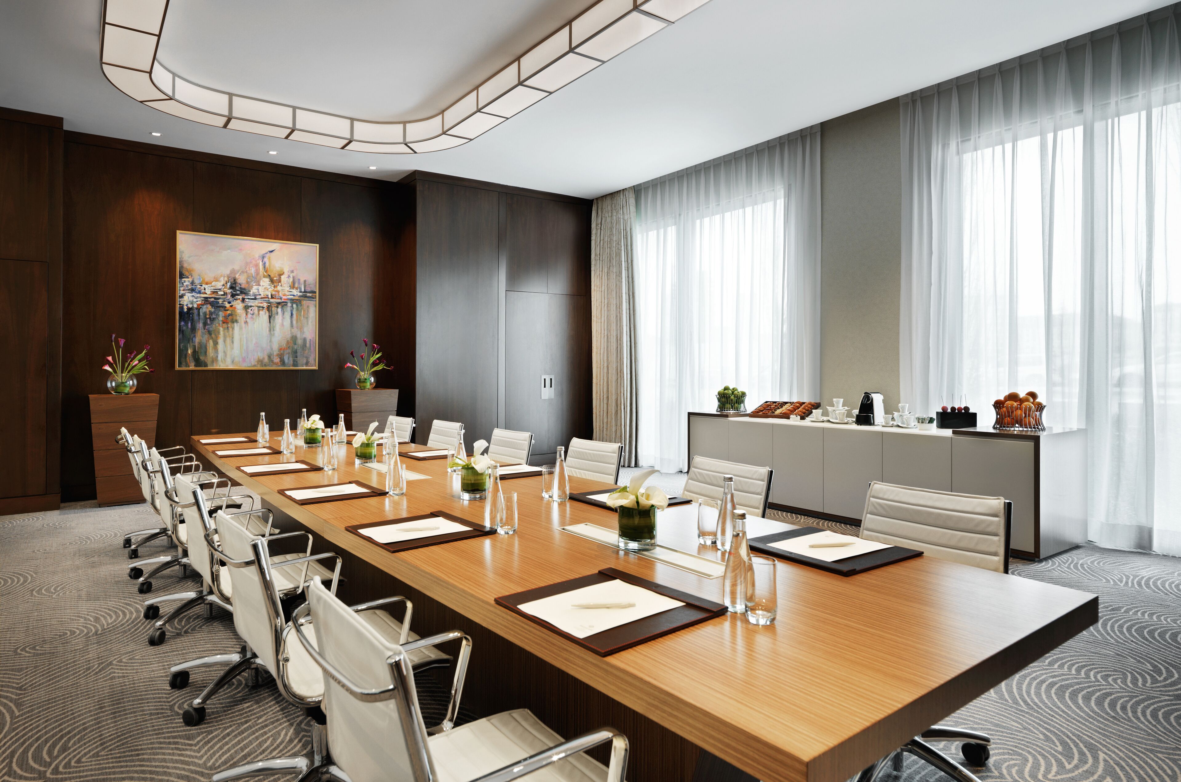 A conference room with a long table, chairs, and a painting on the wall.