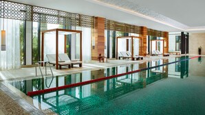Piscina interior moderna com água cristalina, espreguiçadeiras e vista para o verde lá fora.