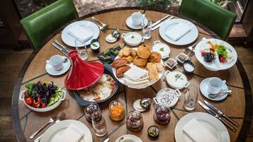 A round dining table with various breakfast items, including eggs, pastries, and salads, surrounded by green chairs.