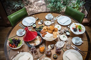 Une table de salle à manger ronde, sur laquelle sont disposés divers aliments pour le petit-déjeuner, notamment des œufs, des viennoiseries et des salades, et autour de laquelle sont placées des chaises vertes.