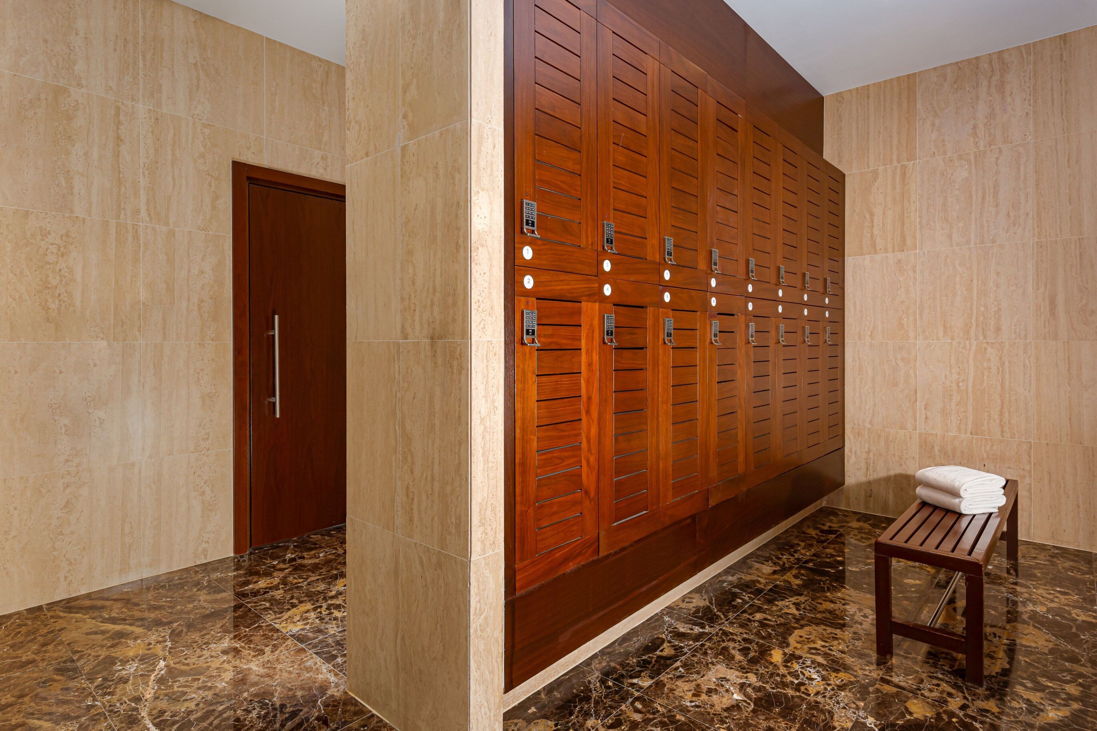 Un baño moderno con piso de mármol, taquillas de madera y un banco de madera, además de una puerta.