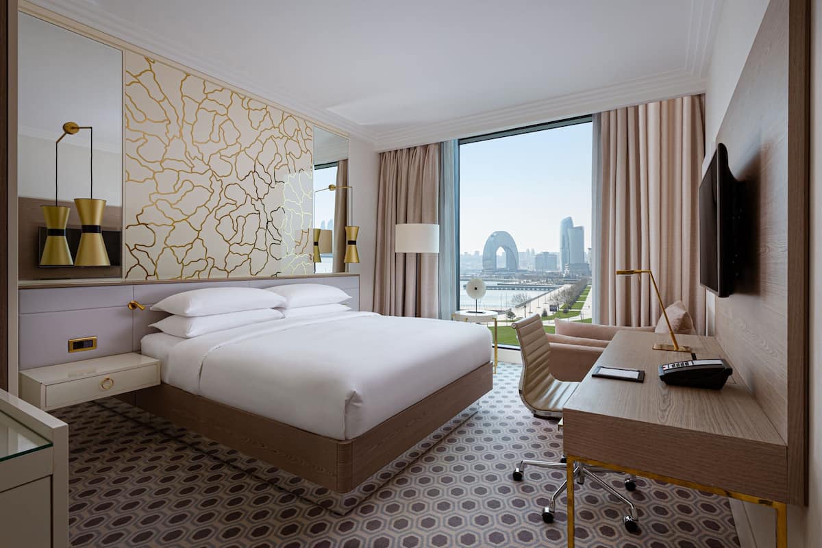 Habitación de hotel con una cama grande, un escritorio con silla, televisión y vista a la ciudad.