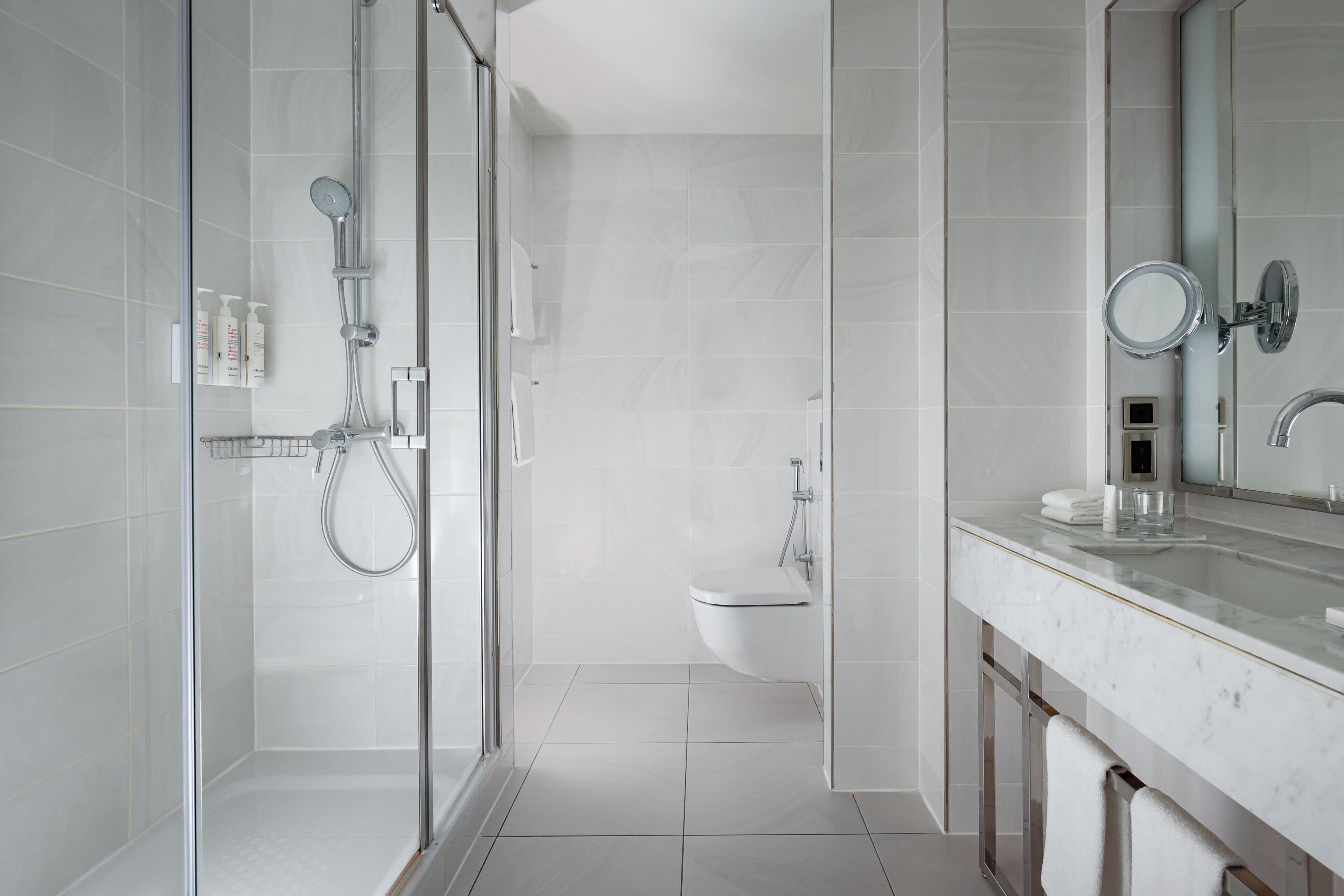 A modern bathroom with a glass-enclosed shower, a toilet, and a marble countertop with a mirror.