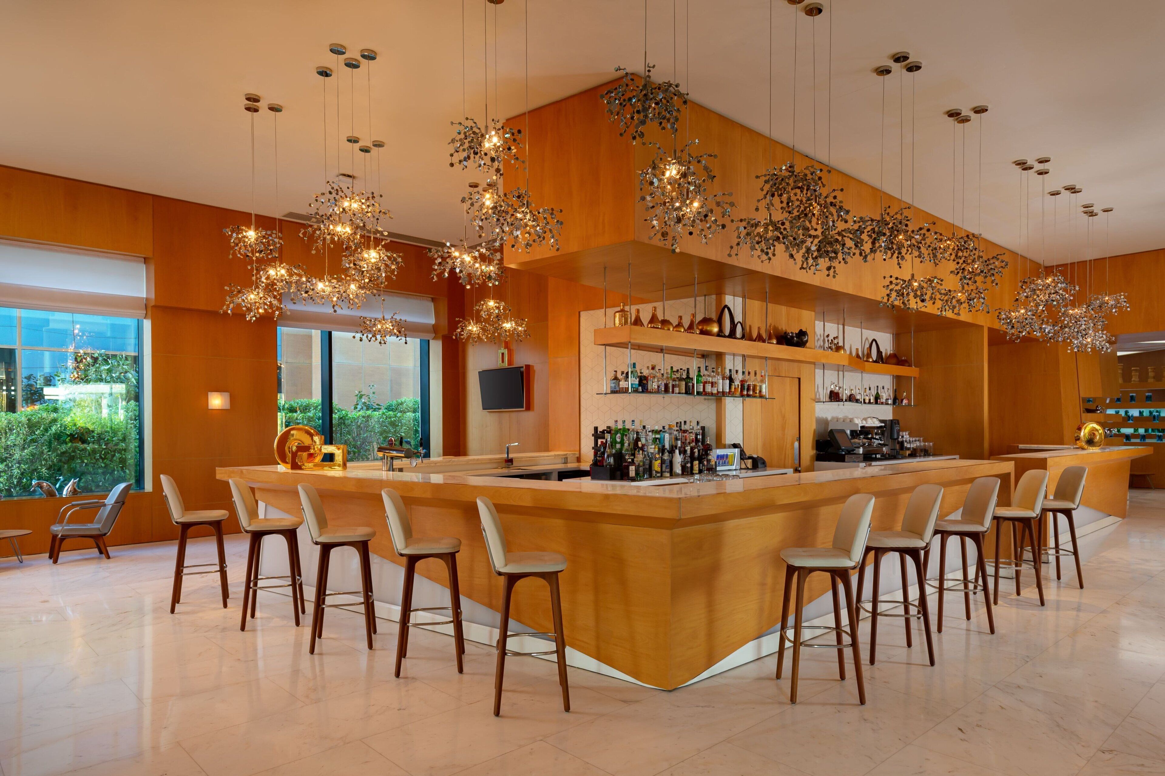 A modern bar area with a central island, bar stools, hanging light fixtures, and shelves with bottles.