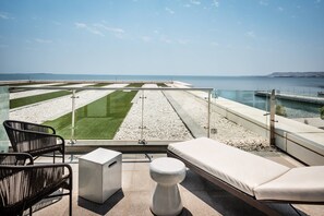 Un balcon avec vue sur la mer, un coin salon avec un canapé et des fauteuils blancs, et une petite table blanche.