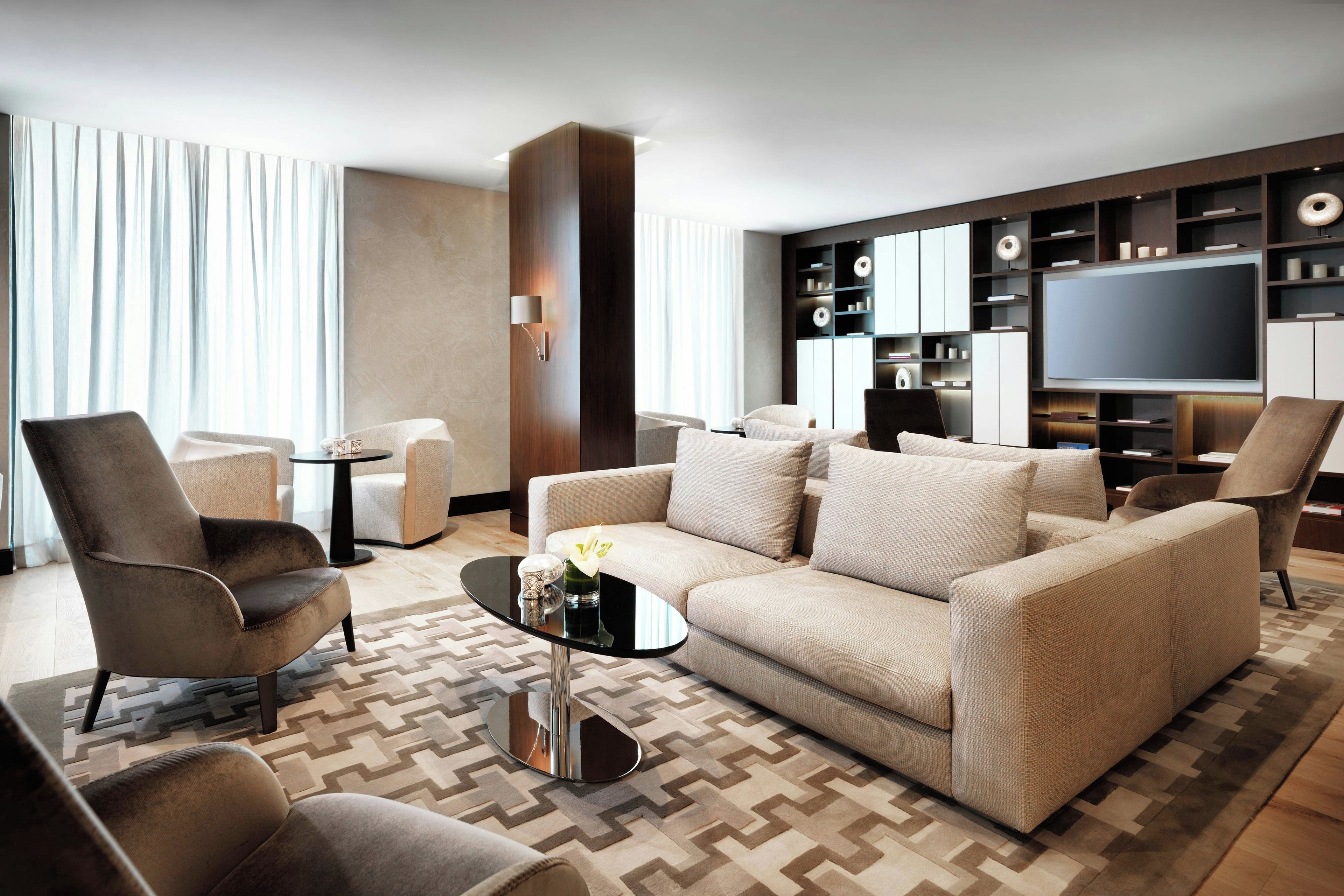 A modern living room with a sofa, armchairs, a coffee table, and a flat-screen TV.