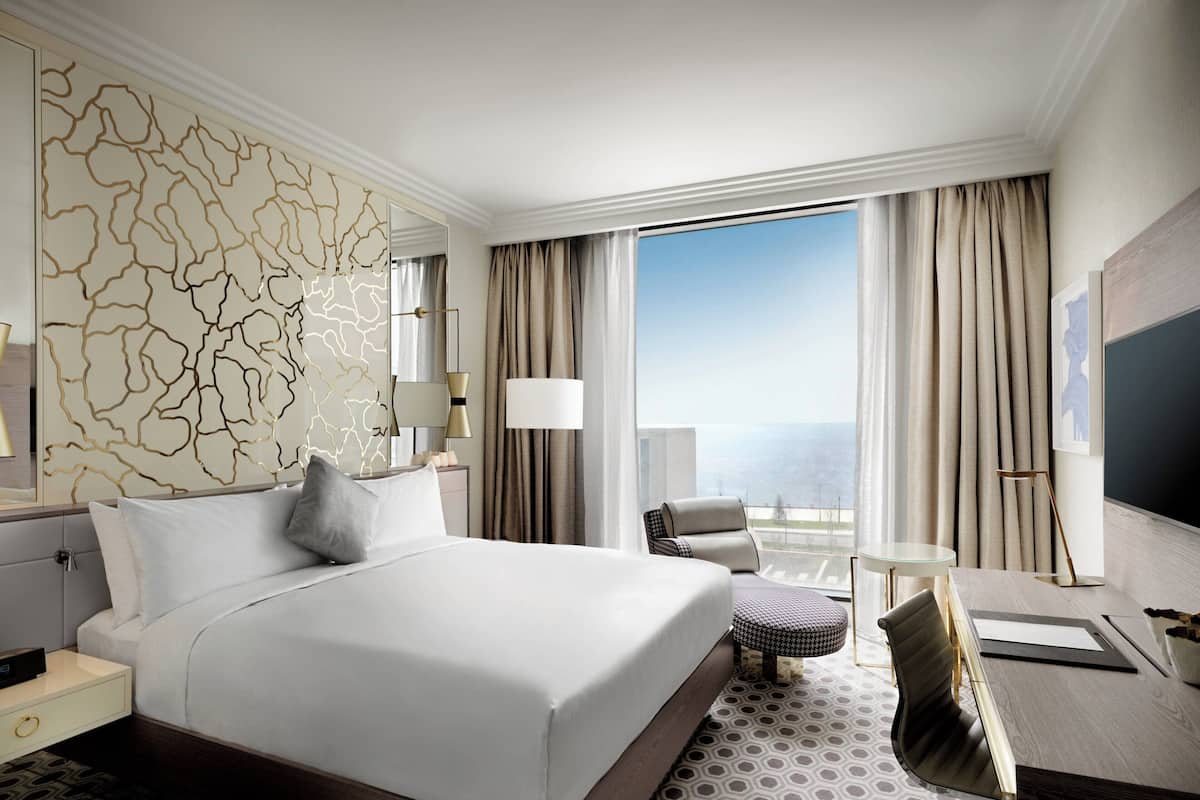 Habitación de hotel con una cama grande, un escritorio, una silla y vista al océano.