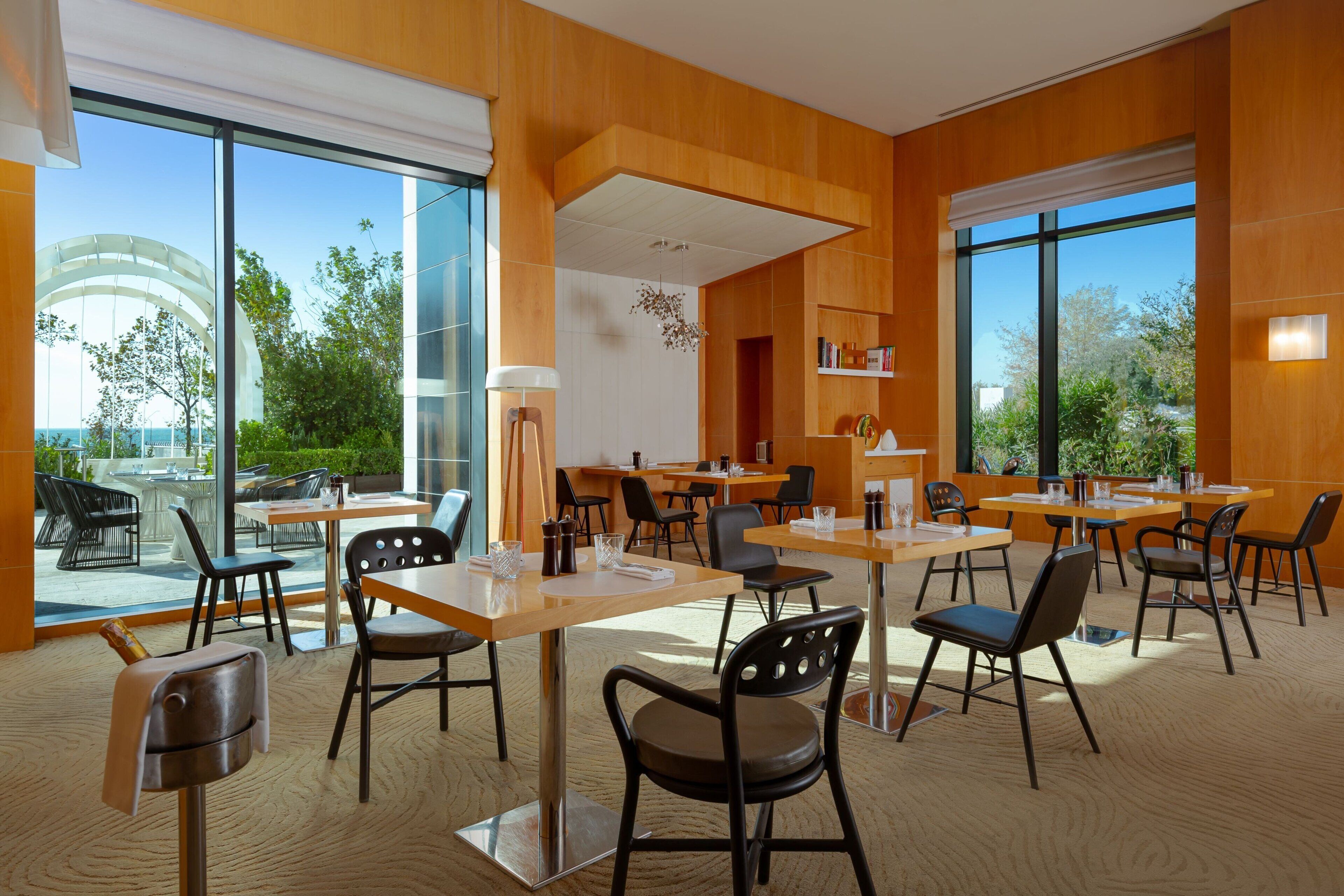A modern dining area with wooden walls, large windows, and a view of greenery outside.