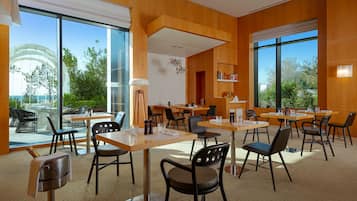 A modern dining area with wooden walls, large windows, and a view of greenery outside.