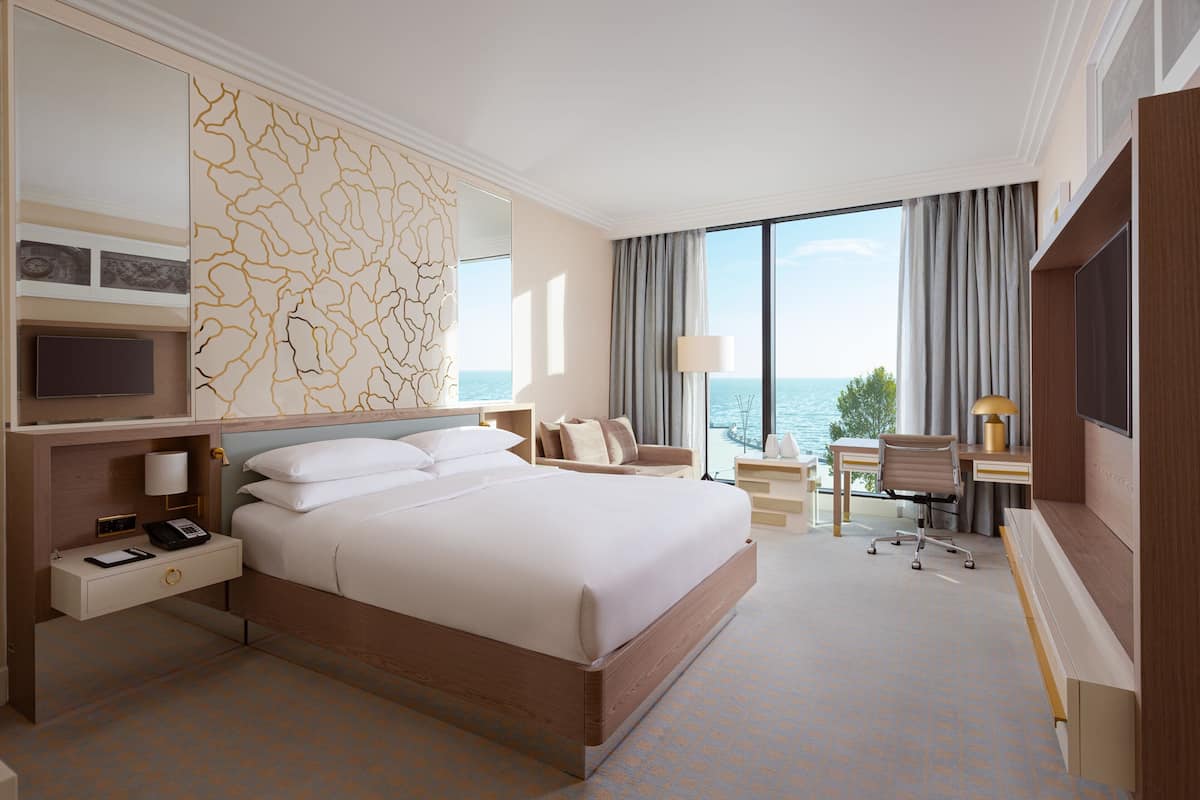 Una habitación de hotel con una cama grande, un escritorio con una silla, un televisor y vista al mar.