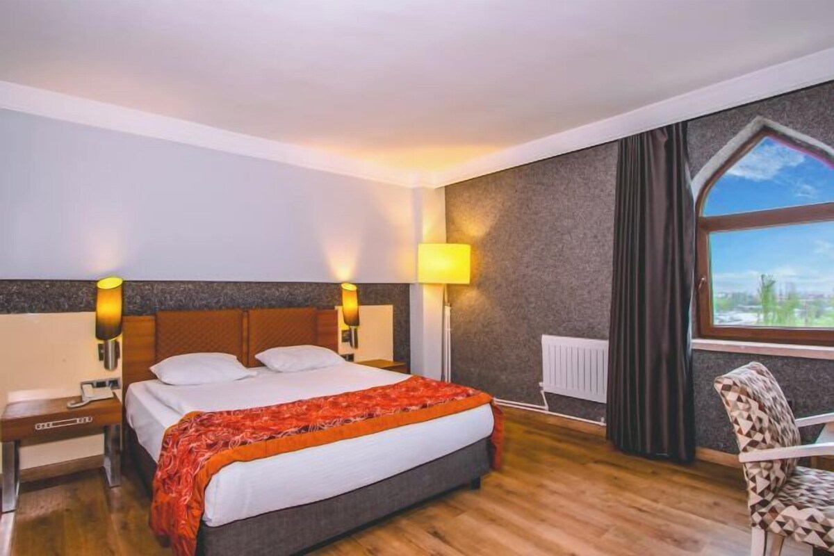 Et hotelværelse med en stor seng, sengeborde med lamper, en stol og et vindue med udsigt.
