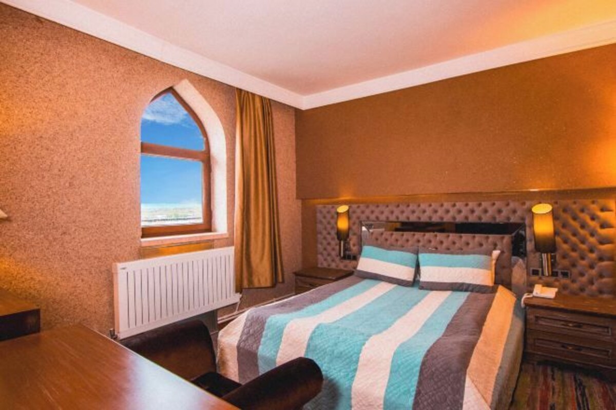 Et hotelværelse med en stor seng, et vindue med udsigt, en radiator og et natbord med lampe.
