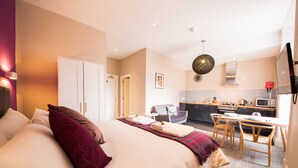 A modern hotel room with a large bed, a small desk, a chair, a kitchen area, and a TV. - The Spires Serviced Apartments Edinburgh (Edinburgh)