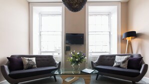 A modern living room with two dark sofas, a glass coffee table, a vase with flowers, and a floor lamp. - The Spires Serviced Apartments Edinburgh (Edinburgh)
