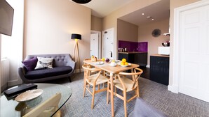 A modern living room with a sofa, a dining table with chairs, a lamp, and a kitchen area with cabinets and appliances. - The Spires Serviced Apartments Edinburgh (Edinburgh)