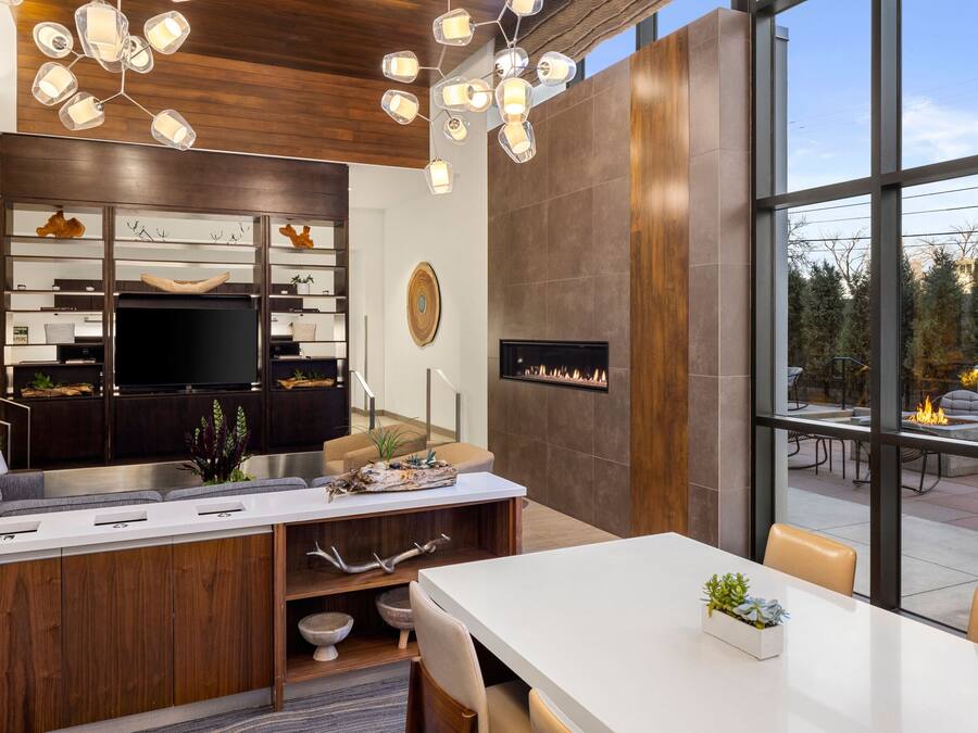 A modern kitchen with a built-in stove, a dining area with a white table, and a view of the outdoors through large windows.