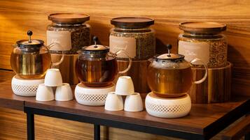 Una mesa de madera con varios dispensadores de té y café, y tazas de cerámica blanca.