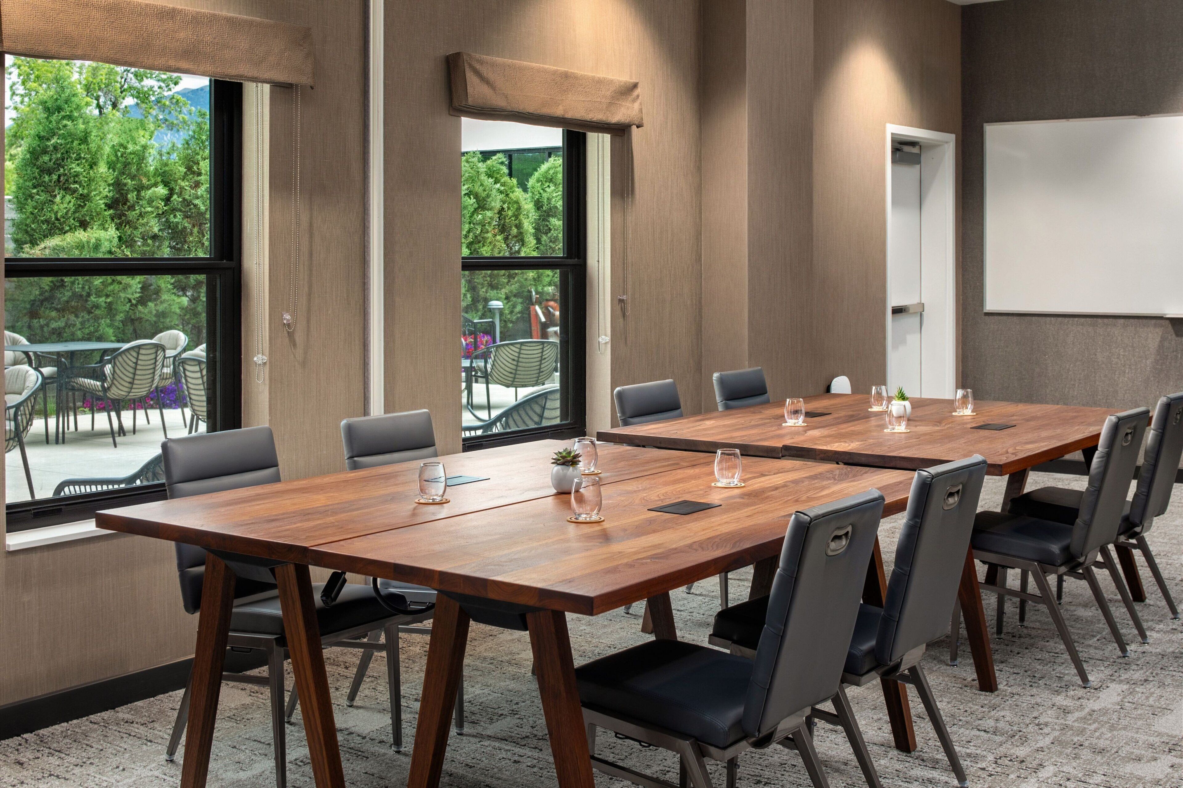 A conference room with two large wooden tables, black chairs, and a whiteboard.