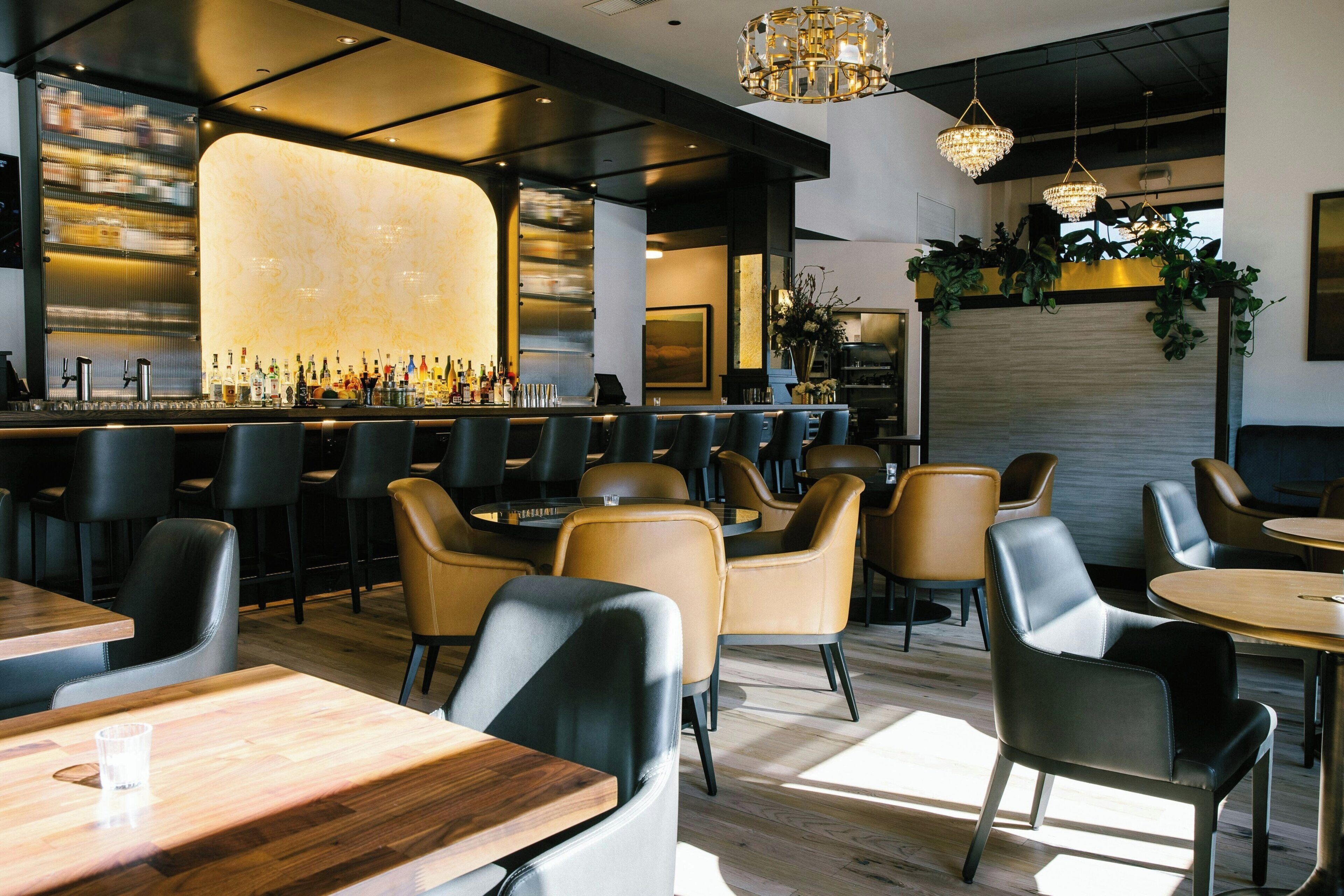 A bar area with a variety of bottles and glasses, bar stools, and a counter.