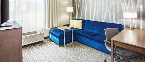 Une chambre d’hôtel avec un canapé bleu, un petit bureau, une télévision et une lampe.