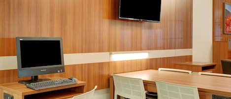 Um espaço de escritório moderno com escrivaninha de madeira, um computador e uma televisão de tela plana fixada na parede.