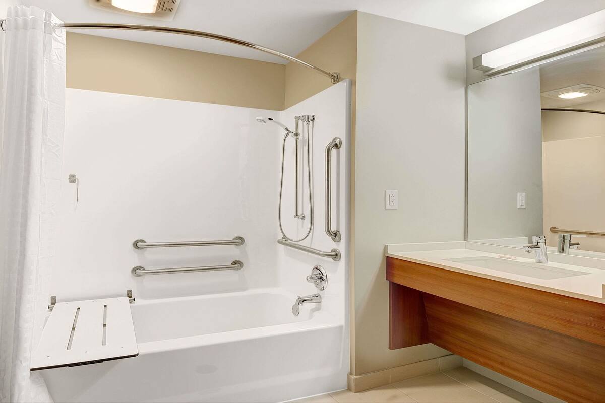 A modern bathroom with a walk-in shower, grab bars, a vanity with a mirror, and a wooden cabinet.