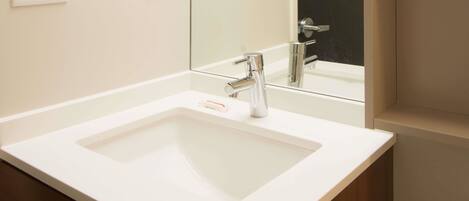 Un baño con lavamanos blanco, un espejo y un mueble de madera.