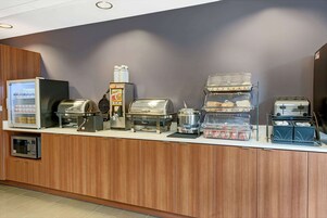 Estación de desayuno autoservicio con microondas, tostadora, cafetera y varios recipientes de comida.