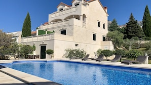 A two-story building with a swimming pool, outdoor seating, and a mountainous backdrop. - Apartments Villa Jadranka - Adults Only (Bol)