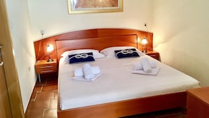 A neatly made bed with towels, a wooden headboard, two bedside lamps, and a framed artwork above. - Apartments Villa Jadranka - Adults Only (Bol)