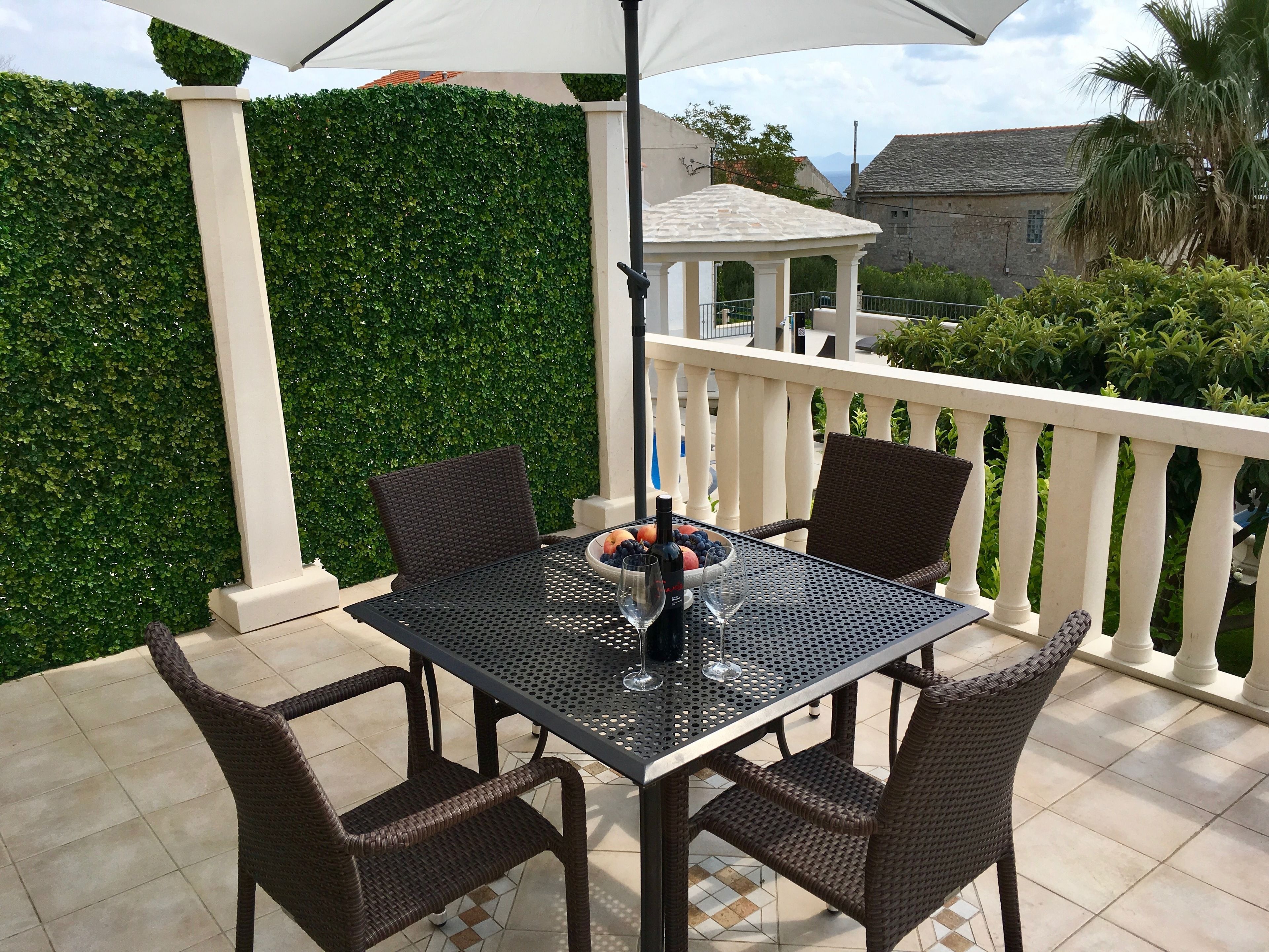 An outdoor patio with a table and chairs, a white umbrella, and a decorative fence.
