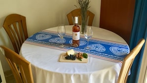 A round dining table with a white tablecloth and a blue patterned table runner. There is a bottle of wine, two wine glasses, and a small wooden board with cheese, grapes, and herbs. - Apartments Villa Jadranka - Adults Only (Bol)