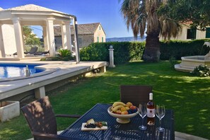 A patio with a table set for a meal, a pool, and a view of the sea. - Apartments Villa Jadranka - Adults Only (Bol)