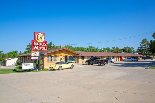 A motel with a large sign, a parking lot, and several cars parked in front. - Sioux Motel (Murdo)