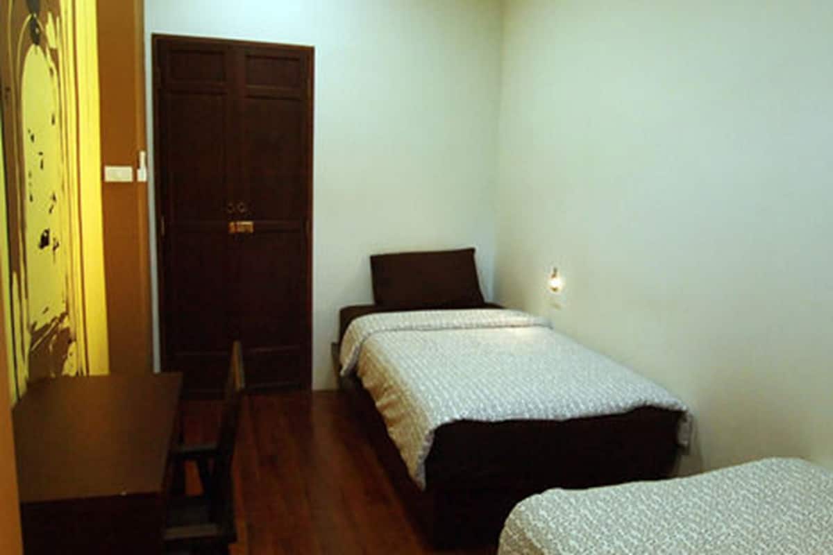Una habitación pequeña y escasamente amoblada con una cama individual, una silla y una puerta de madera.
