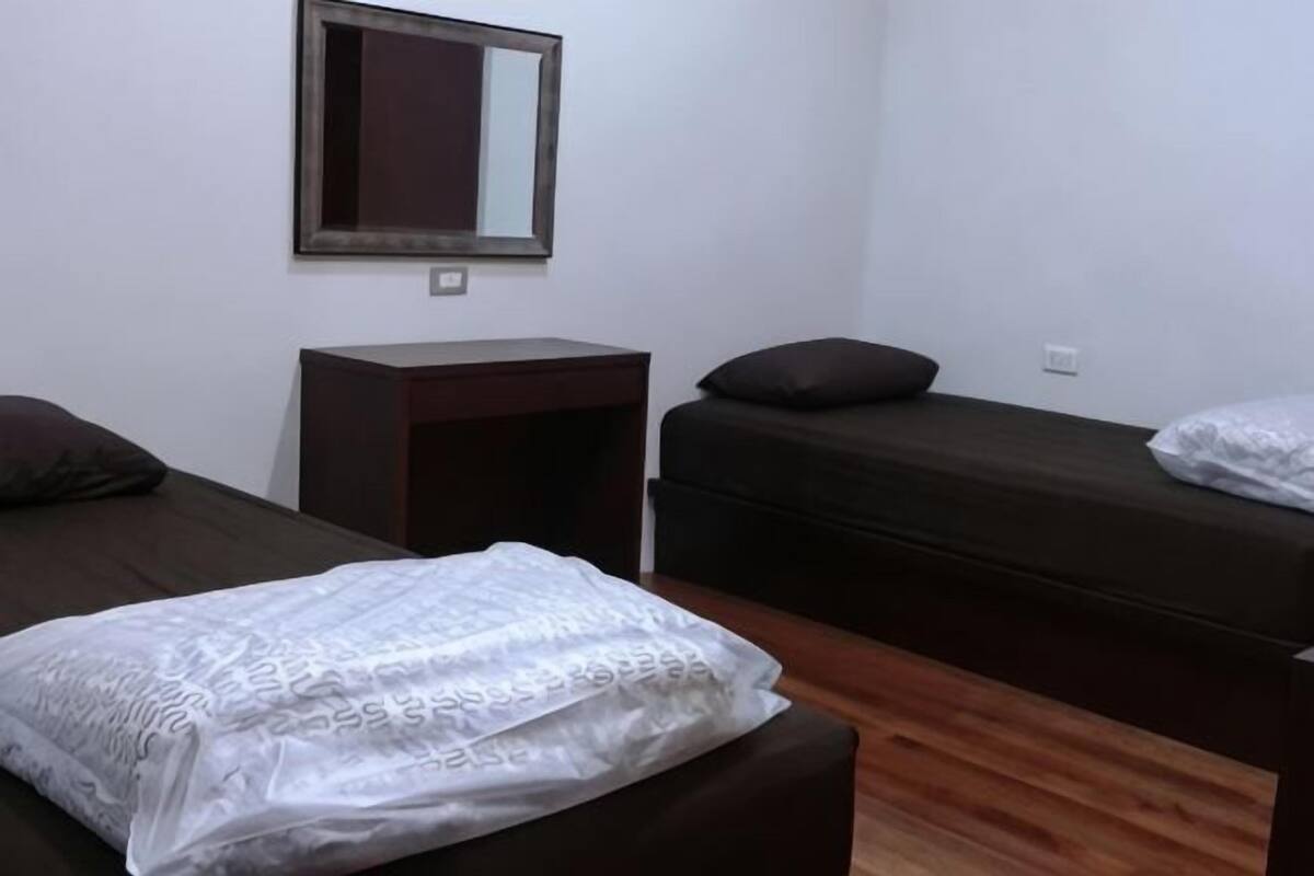 Una habitación con dos camas, una mesita, un espejo y una toma de corriente.